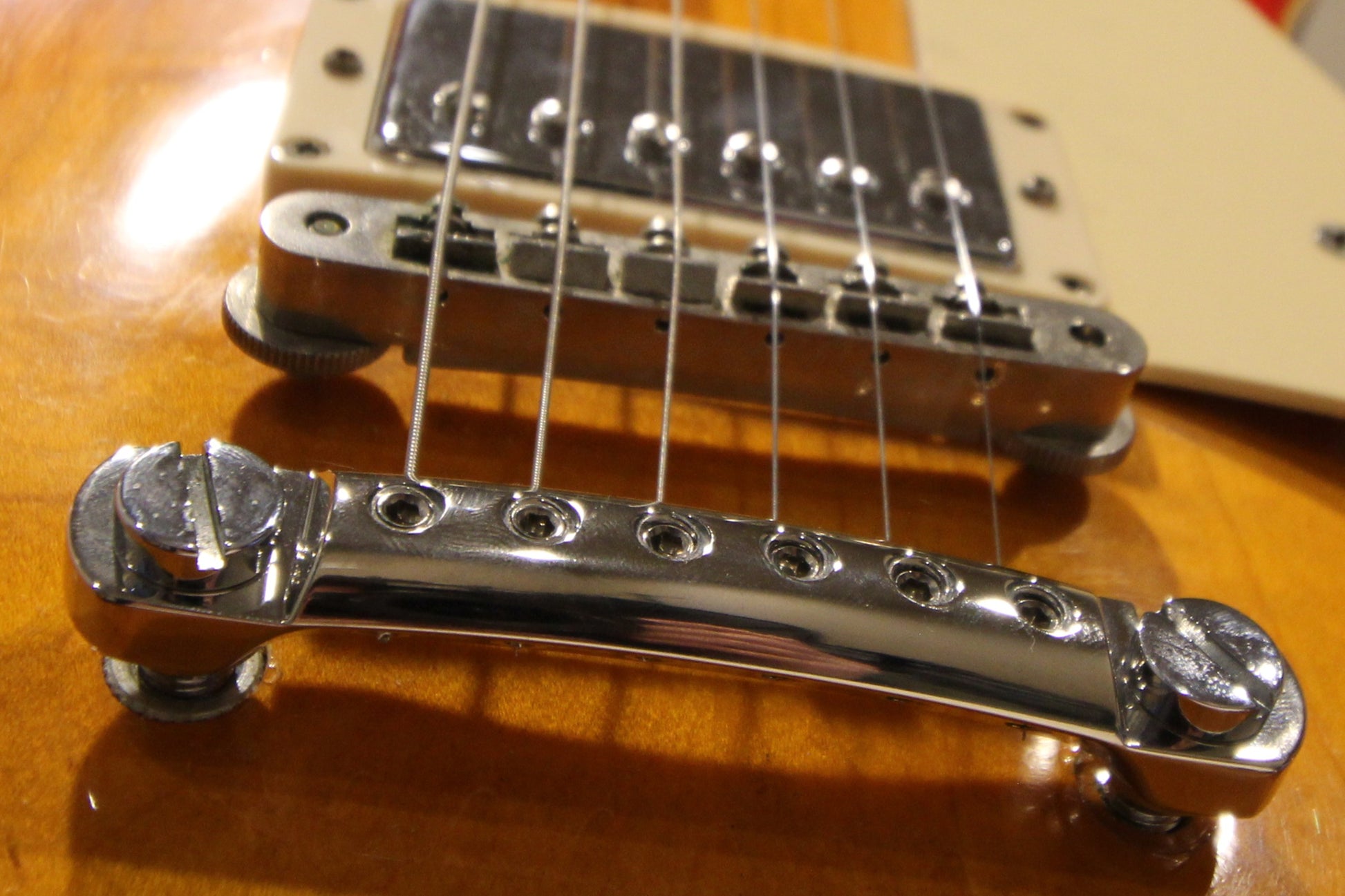 Close-up of polished nickel CNC aluminum stopbar on guitar detailing mounting hardware, bridge, and pickup